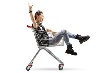 Punk girl riding in shopping cart and making rock gesture