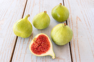 Whole figs and one fig sliced in half on top of a  garden table. Focus is on the sliced fig.