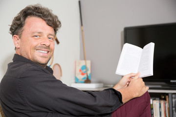 Man reading book sitting on a comfortable couch at home