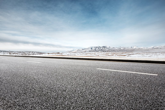 empty asphalt road near snow mountains in blue sky