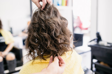 Naklejka premium Beautiful curly hairstyle of brunette young woman in hair salon. 