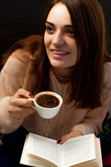 A young beautiful girl in a warm sweater drinks coffee and reads a book, a cute portrait