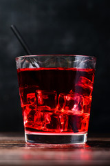 Top view of glass of red cocktail with ice cubes and straw on dark wooden table, close-up