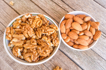 Two ceramic bowls full of walnuts and almonds on the wooden background