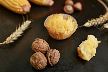 Yellow muffin on black table with wallnuts, corn and wheat