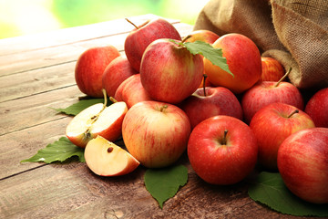 Ripe red apples with leaves on wooden background