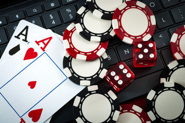 Naklejka premium Internet casino and online gambling concept with two cards (aces) on a keyboard, dice used to play the game of craps, black and red poker chips and a laptop