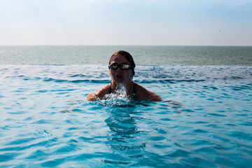 Girl in glasses in a swimming pool with sea view