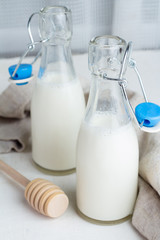 Milk in small glass bottles, honey and honey stick.