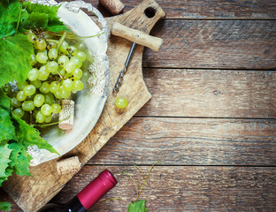 Grapes,a bottle of wine, corks and corkscrew on a wooden old table, rustic style