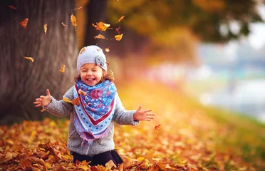 Poster adorable happy girl playing with fallen leaves in autumn park © Olesia Bilkei