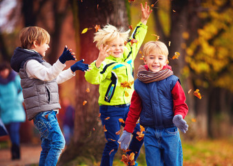 happy friends, schoolchildren having fun in autumn park among fallen leaves