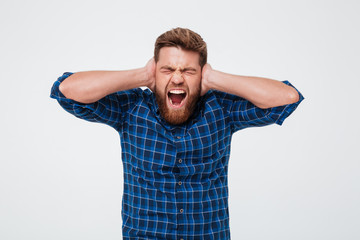 Portrait of an irritated bearded man covers his ears