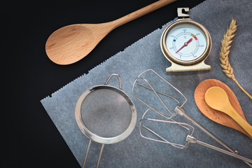 Bakery preparation tools wooden spoon, vanilla, thermometer, bake paper on black background