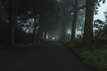 Misty country road with tractor and illuminating headlights.