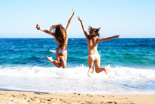 Back view of girls in bikini jumping on beach