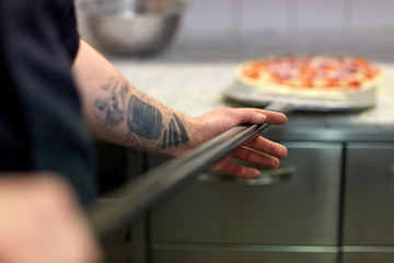 cook or baker hand with pizza on peel at pizzeria