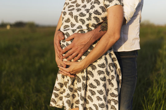 Midsection of man touching pregnant woman stomach while standing  on grassy field