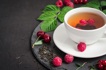 Berry tea and ripe raspberry, cherry, currant on a black background