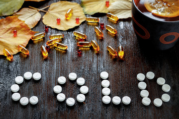 Concept of cold autumn - pills, leaves on dark wood