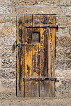 Old weathered yellow wooden door in stone wall