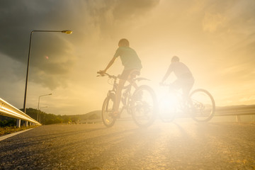 Peple biking on road with sunset silouette background.