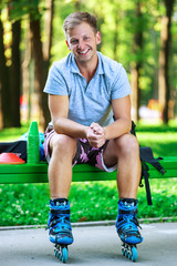 Portrait of happy handsome male roller sitting on bench in the park.