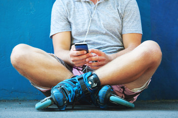 Inline roller skater with phone sitting against blue wall.