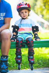 Portait of cute baby boy with  inline skates sitting on bench.