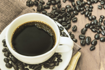Black coffee in white cup and coffee bean on wooden table