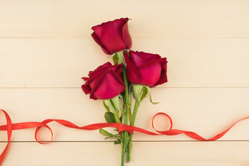 Red roses bouquet decorated with red ribbon on light wood background 