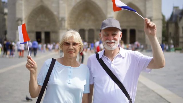 Happy cheerful family enjoying vacation. Seniors standing near Notre-Dame de Paris. Holding french flags in hands, waving it