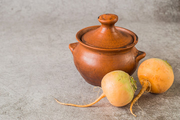 Fresh raw yellow turnip and brown clay pot and  on a gray background. Preparation of steamed turnips.