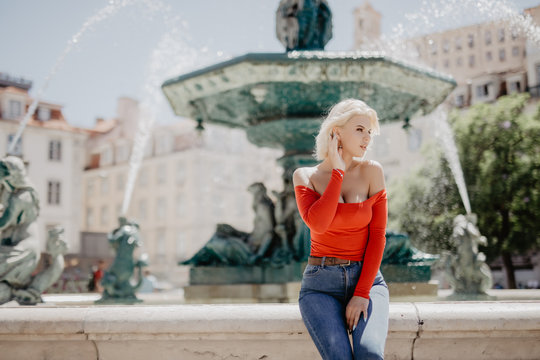 Close-up portrait of a blond girl with blonde hair posing in park on fountain background.