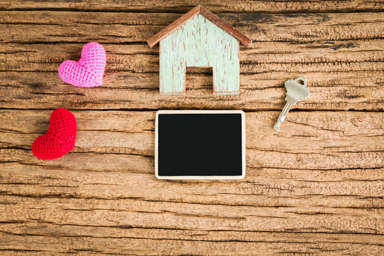 A wooden home and red heart for family and blackboard for ad text and house key put on the wood, Loan for real estate and advertising business concept.