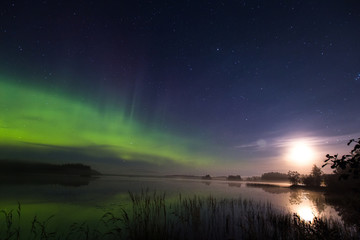 Fototapeta na wymiar Aurora borealis and full moon rich colors above lake in Finland