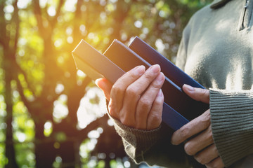 Woman holding pile of books out door. Close up of female holding books.