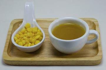 Water the corn in a white cup and corn kernels in a white spoon.