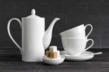 White porcelain coffee pot, stacked cups and sugar cubes on wooden rustic table.