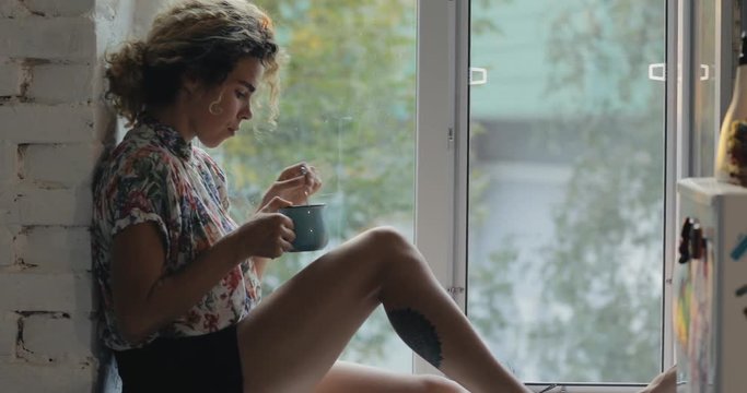 Curly hair woman enjoy hot tea sitting on windowsill in autumn day