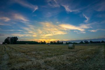 Fototapeta premium Beautiful colorful orange sunset over field with hay bales and blue sky