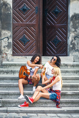 Group of young female friends sitting on the stairs singing and playing guitar.