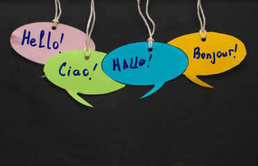 Hello / Speaking learning foreign languages. colorful speech bubbles hanging from a cord on blackboard background © Oleksandr