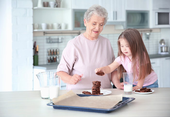 Cute little girl and her grandmother with cookies on kitchen