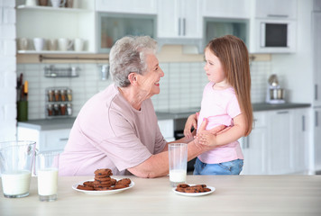 Cute little girl and her grandmother with cookies on kitchen