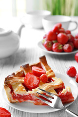 Plate with delicious piece of strawberry pie on wooden table