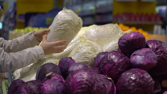 A woman chooses cabbage on a vegetable shelf. The concept of purchasing vegetables and fruits in a supermarket.