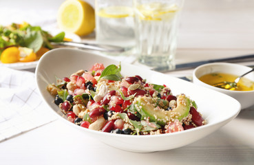 Superfood salad with avocado, beans and pomegranate seeds in white bowl on kitchen table