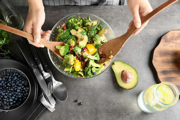 Woman mixing delicious superfood salad ingredients with wooden spoons in kitchen