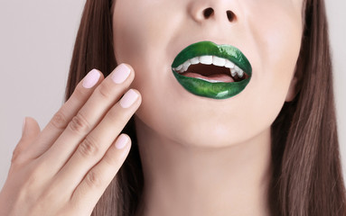 Young beautiful woman with fancy green lipstick on color background, closeup